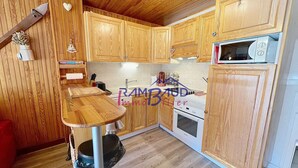 Une cuisine avec des meubles de rangement en bois, un four à micro-ondes, une cuisinière et une poubelle.
