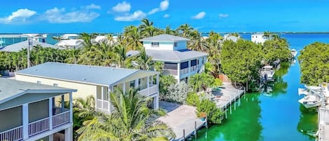 A coastal residential area with houses along a narrow waterway, surrounded by lush greenery and palm trees.