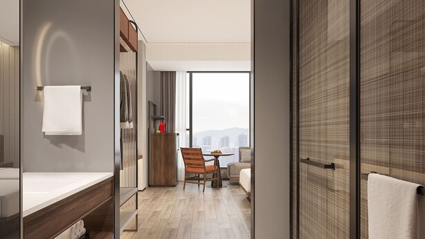 Een moderne hotelkamer met een groot raam, een houten stoel, een klein tafeltje en een badkamer met een handdoekhouder.
