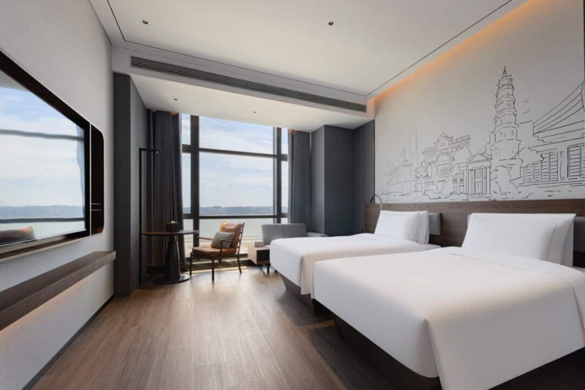 A hotel room with two beds, a view of the city, and a large window.