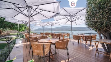 An outdoor dining area with tables and chairs, umbrellas, and a view of a lake and mountains.
