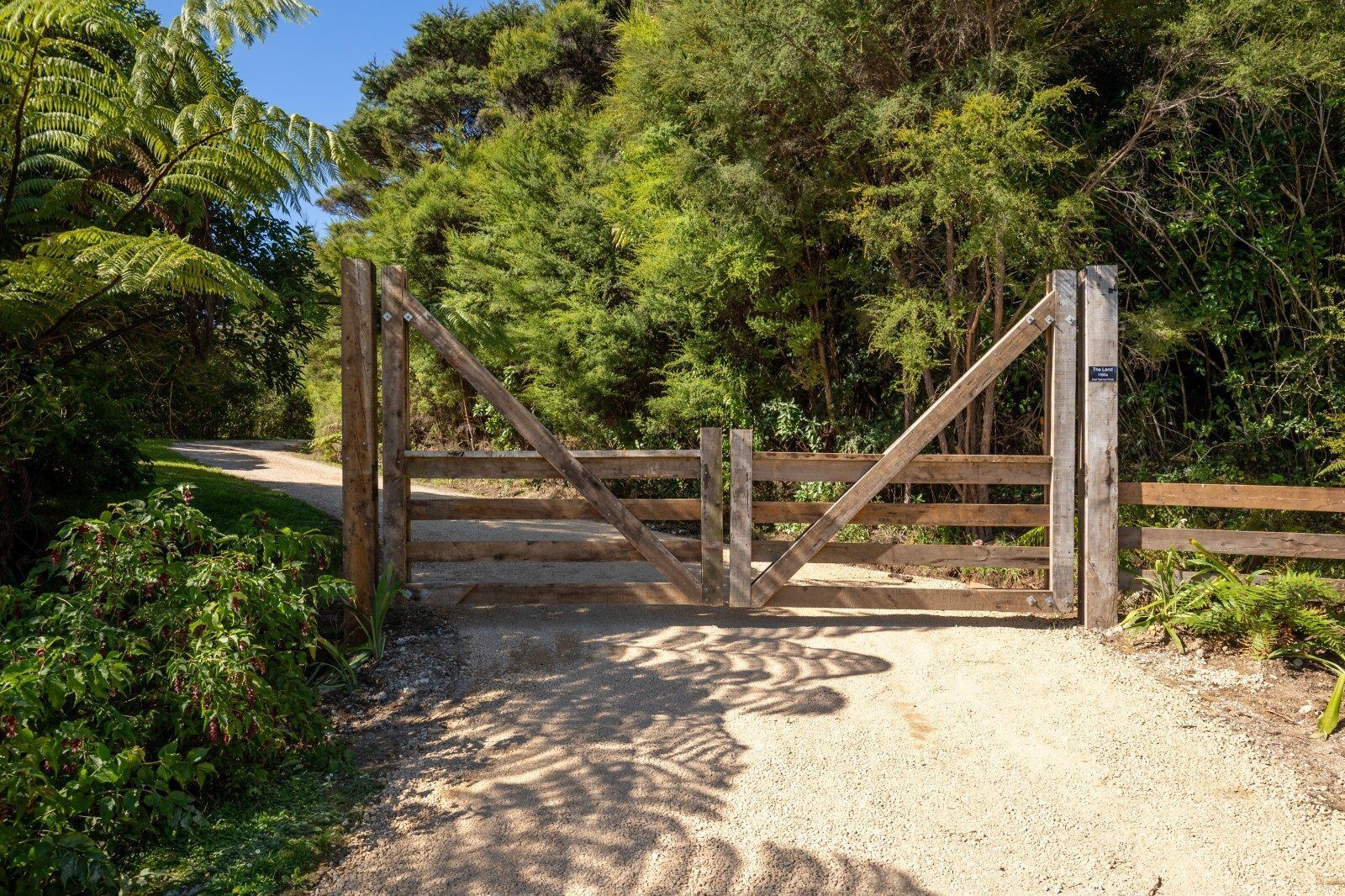 Une porte en bois, située dans une zone boisée, est traversée par un chemin de gravier.