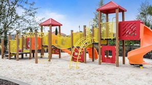 A playground with a yellow slide, red climbing structures, and a red canopy.
