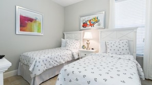 A bedroom with two beds, a nightstand with a lamp, and artwork on the walls.