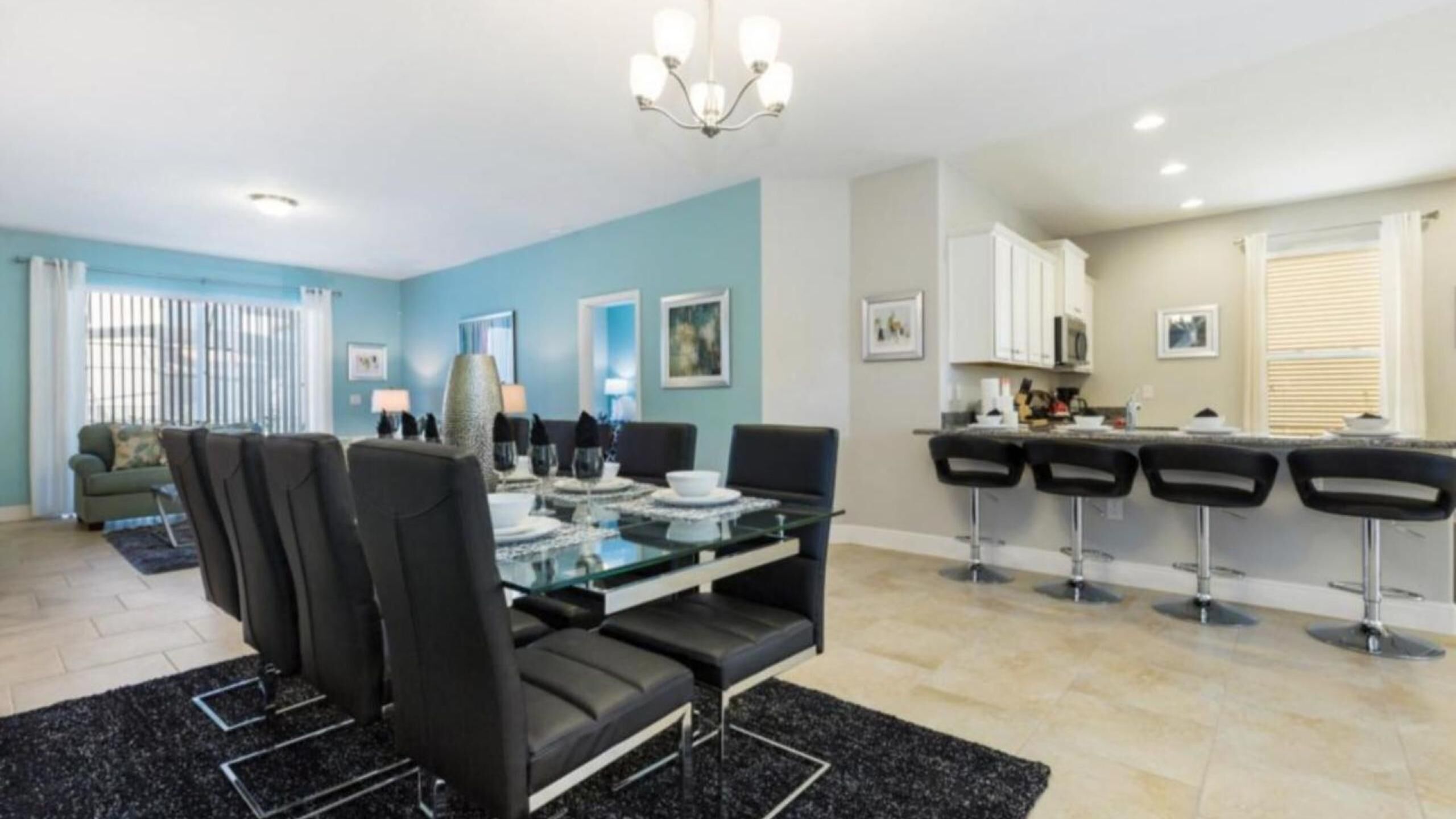 A modern living room with a glass dining table, black chairs, and a blue accent wall.