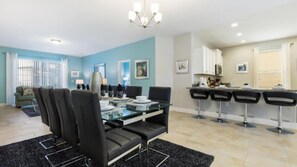 A modern living room with a glass dining table, black chairs, and a blue accent wall.