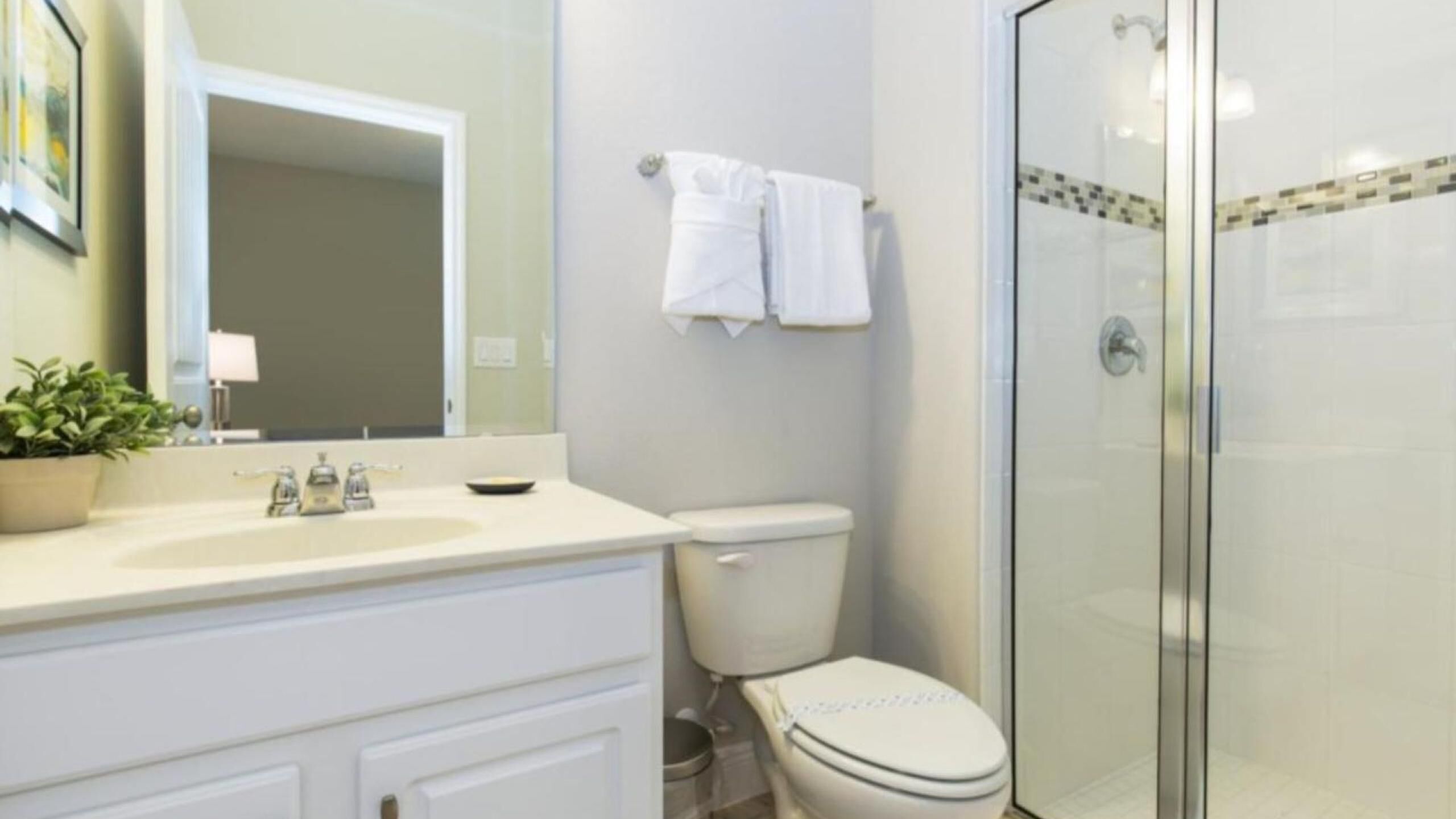 A bathroom with a white sink, mirror, and toilet. There is a shower area with a glass door.