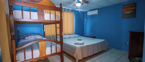 A room with a bunk bed, a single bed, a ceiling fan, and a window with curtains.