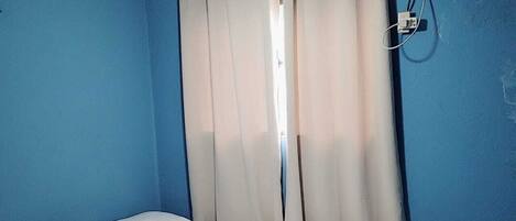 Un dormitorio con cama, cortinas, ventilador de techo y aire acondicionado.
