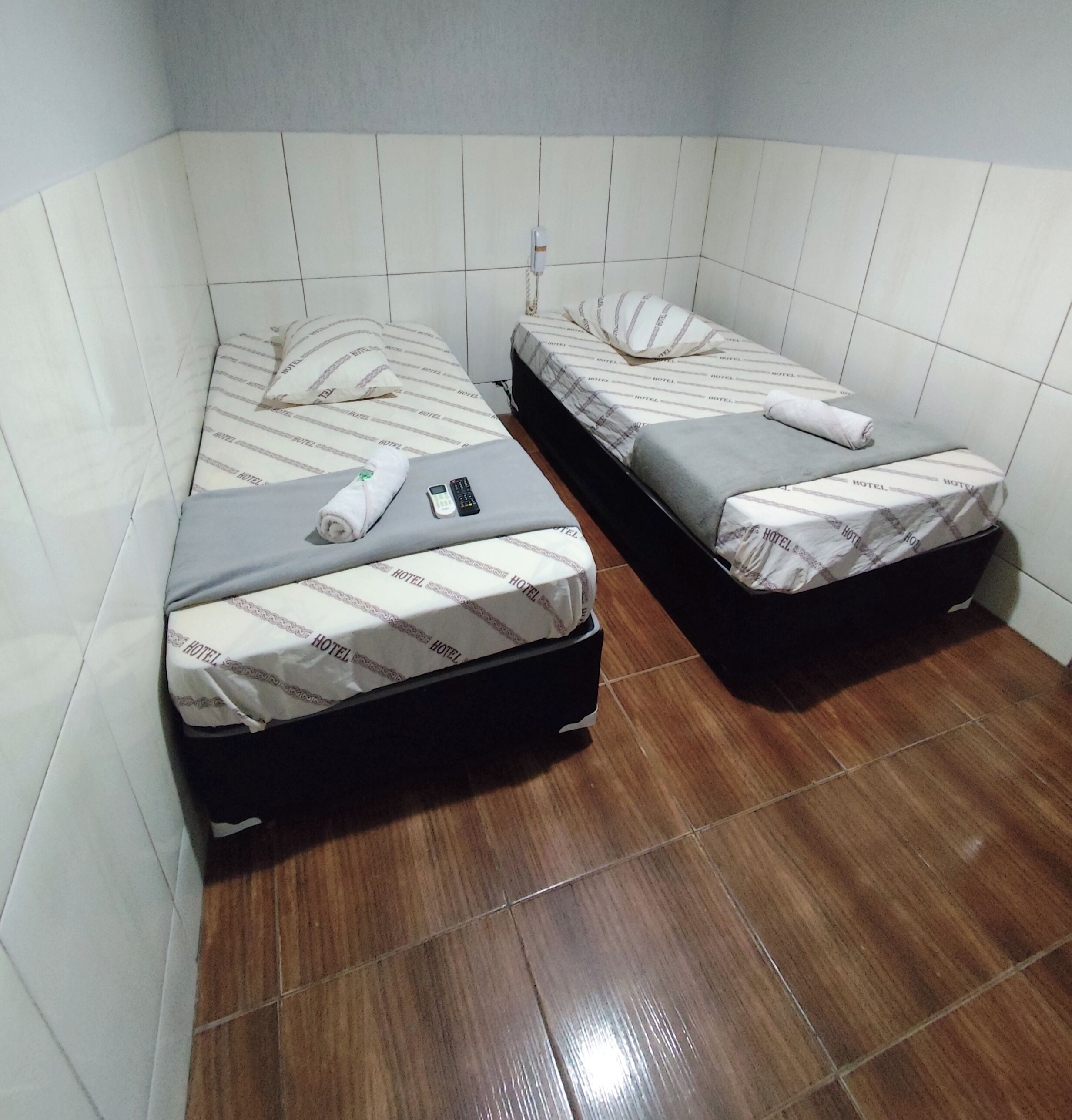 Una camera d'albergo piccola con due letti singoli, ognuno con un cuscino e una coperta.
