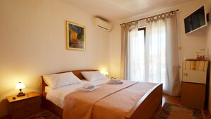A well-lit bedroom with a large bed, a bedside table with a lamp, a wall-mounted TV, and a refrigerator. - Sleek and Serene Flat and Rooms (Rovinj)