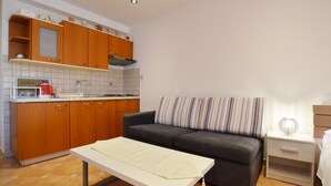 A compact living space with a kitchenette, a sofa, a small table, and a bedside table with a lamp. - Sleek and Serene Flat and Rooms (Rovinj)