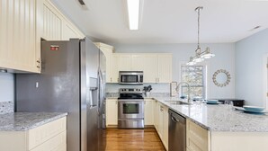 A modern kitchen with a stainless steel refrigerator, a microwave, an oven, and a dishwasher. - Dog Friendly Home with New Pool & Fun Game Room w/ Outside Tiki Bar & Ping Pong (Oak Island)