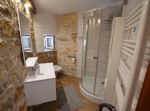 A bathroom with a stone wall, a white sink, a toilet, and a glass shower enclosure. - Urban and Upscale Homes Rovinj Old Town (Rovinj)