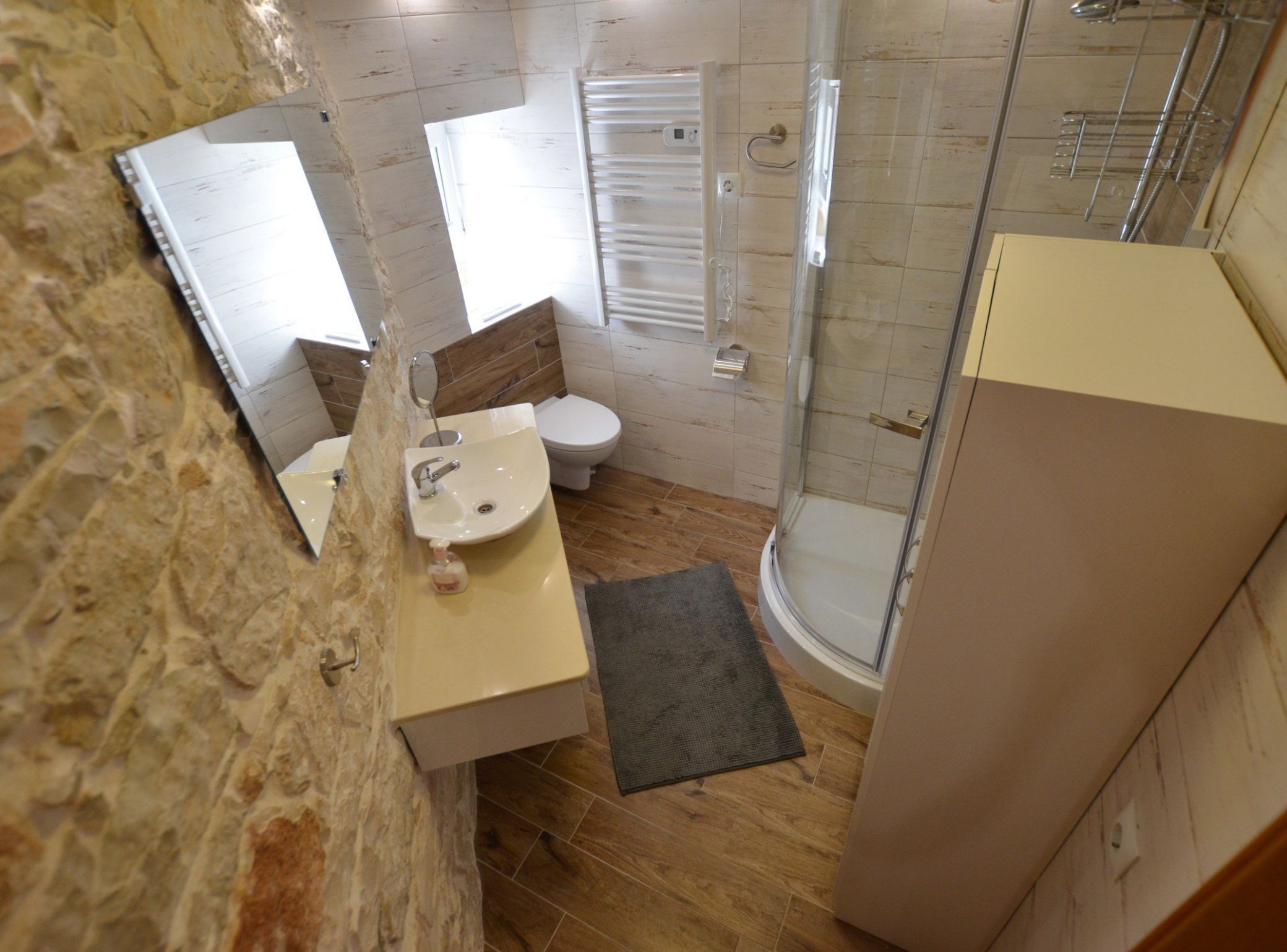 Bagno con parete in pietra, lavandino, WC, doccia e specchio.