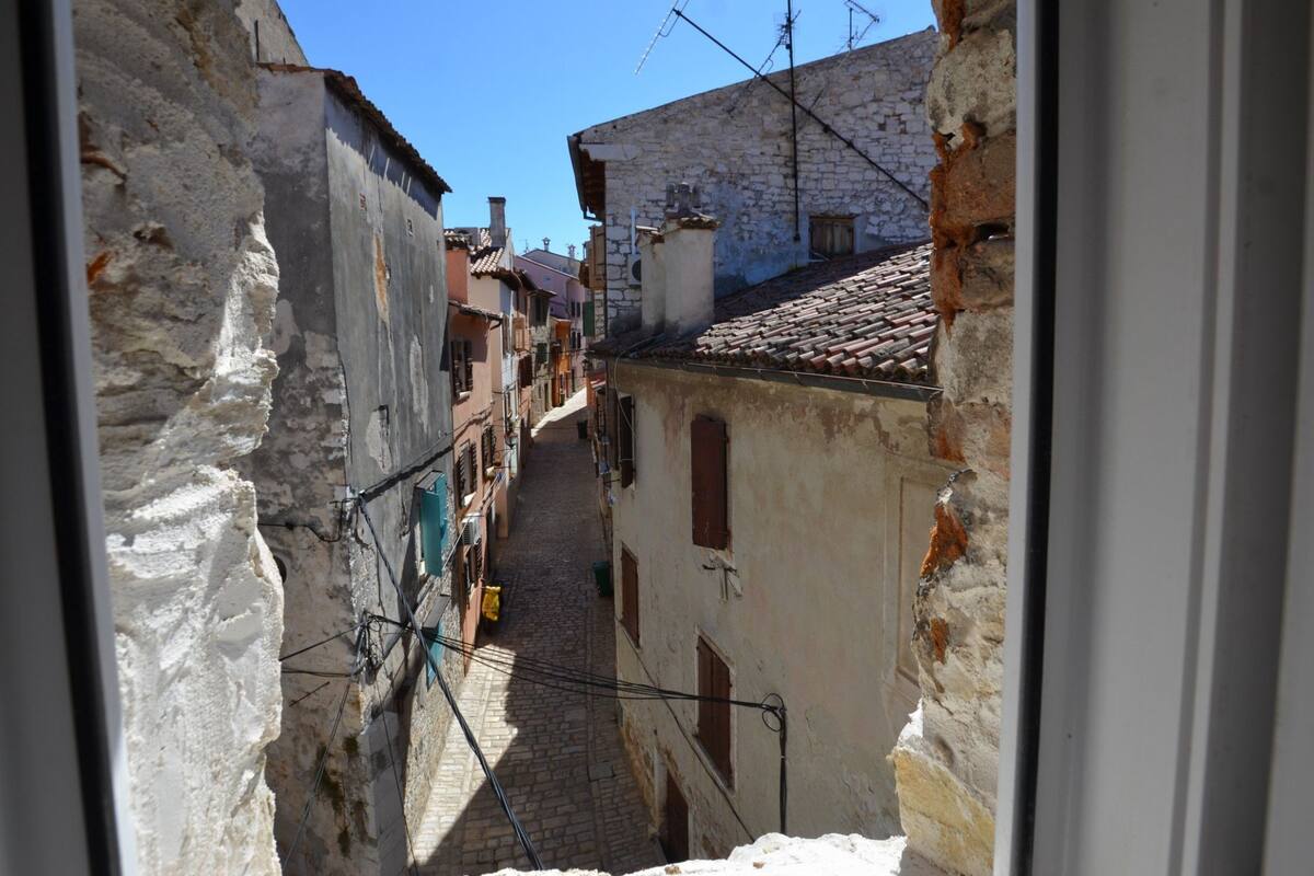 A narrow cobblestone street between old stone buildings with visible chimneys and antennas.