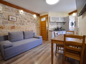 A cozy living room with a stone wall, a light blue sofa, and a wooden dining table with chairs. - Urban and Upscale Homes Rovinj Old Town (Rovinj)