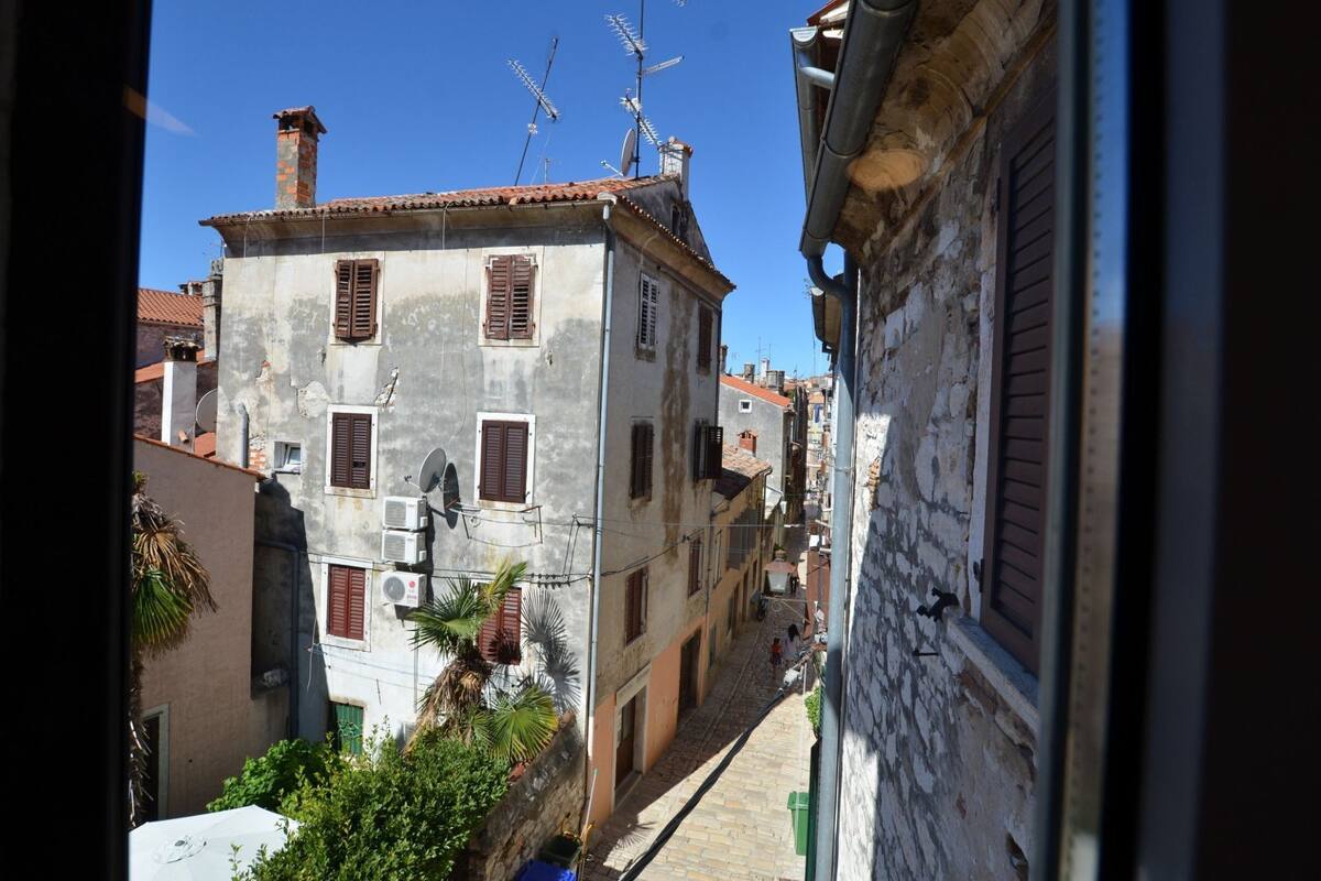 A narrow street with buildings featuring traditional architecture, including visible satellite dishes and antennas.