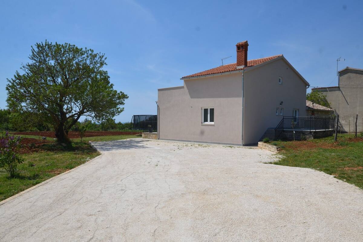A single-story house with a tiled roof, a small window, and a paved driveway.