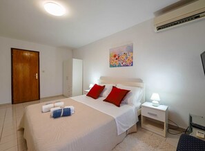 A hotel room with a bed, a nightstand, a desk, an air conditioner, and a door. - Calm and Stylish Rooms With Balcony (Rovinj)