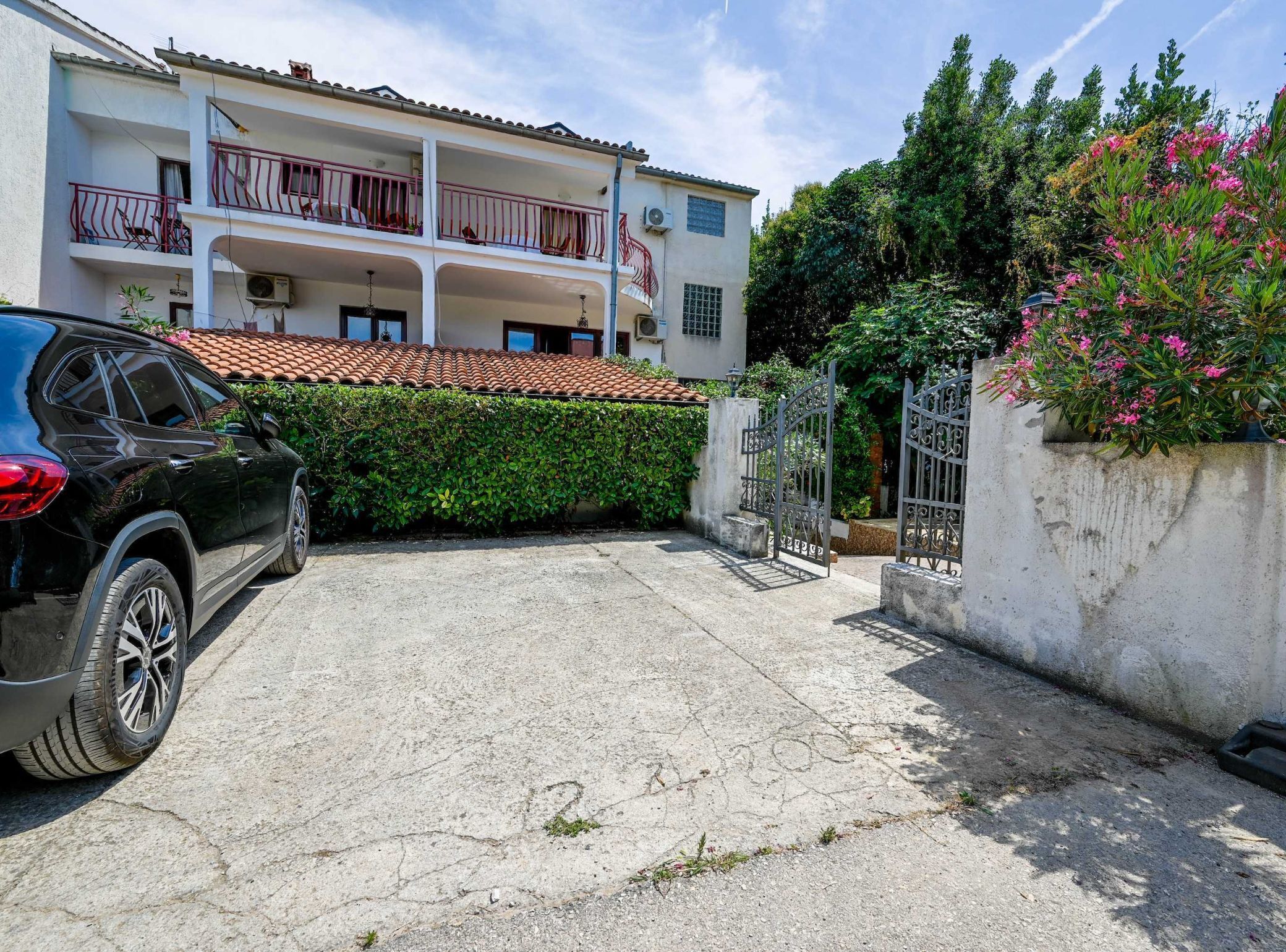 A two-story building with a tiled roof, a balcony with a metal railing, and a car parked in the driveway.