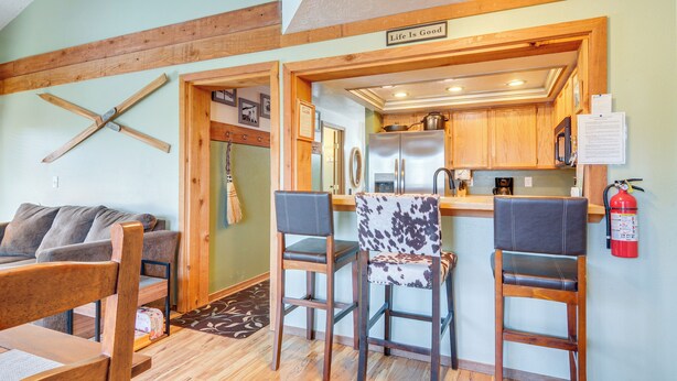 A cozy living area with a wooden ceiling, a kitchen with wooden cabinets, and a bar area with two chairs. - Mtn-View Condo w/ Trail Access in Brian Head (Brian Head)
