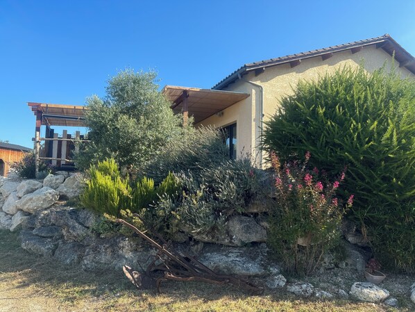 A house with a stone wall, a wooden deck, and various shrubs and plants.