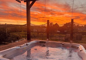 A hot tub with a wooden deck and a netted enclosure, set against a sunset backdrop.