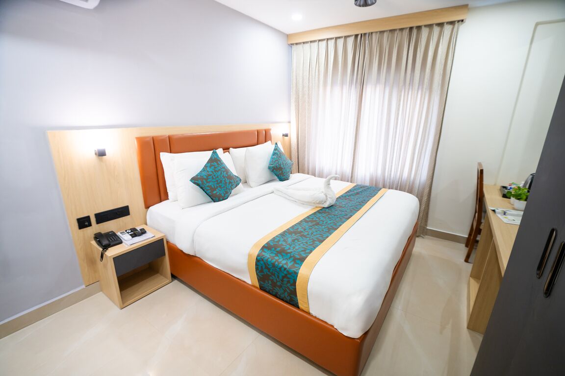 Habitación de hotel con cama, mesita de noche con teléfono, escritorio con silla y ventana con cortinas.