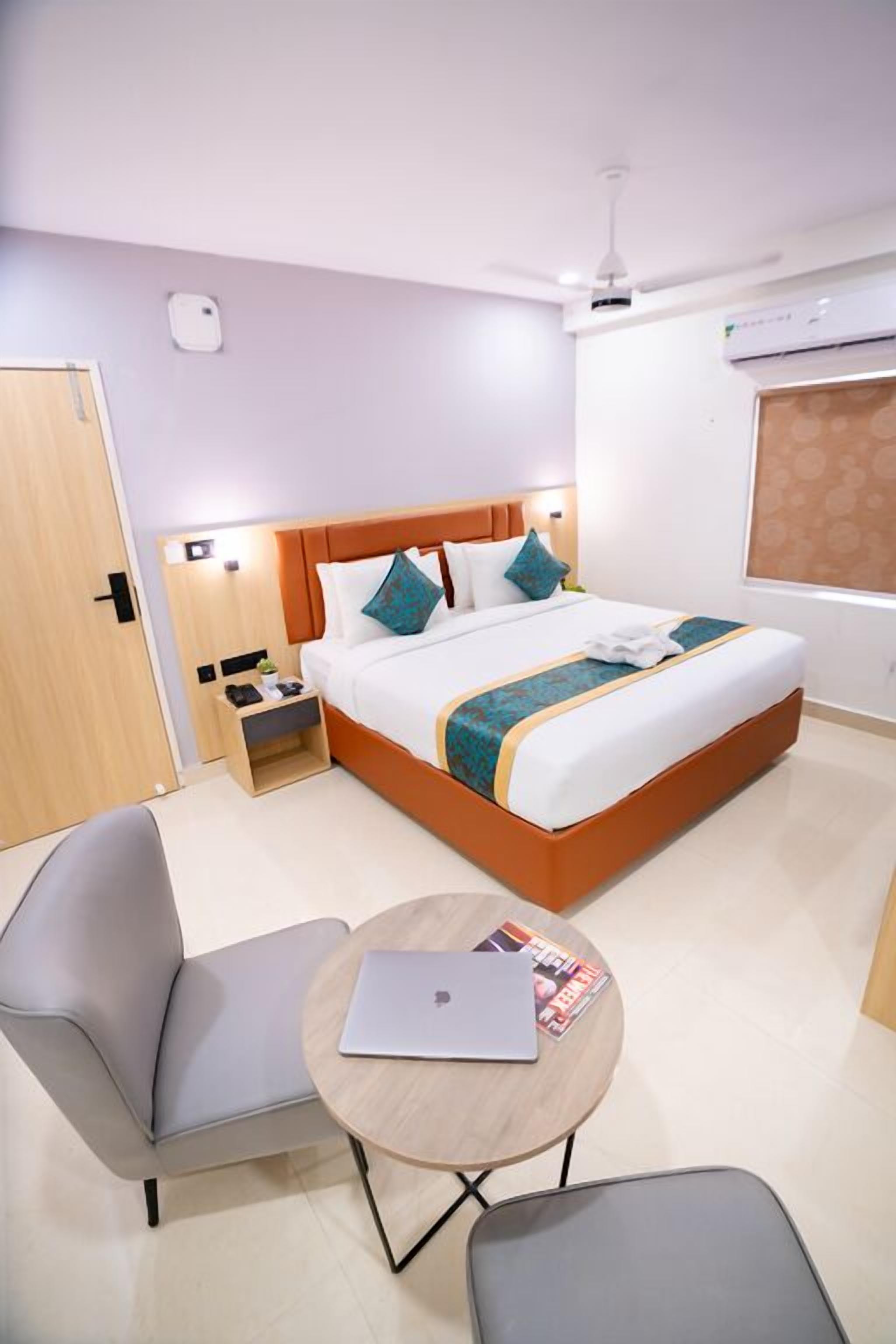 A modern hotel room with a bed, a desk, a chair, and a small table.