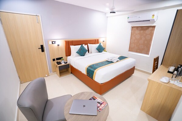 Habitación de hotel con cama, escritorio, silla, ordenador portátil y ventana con persianas.