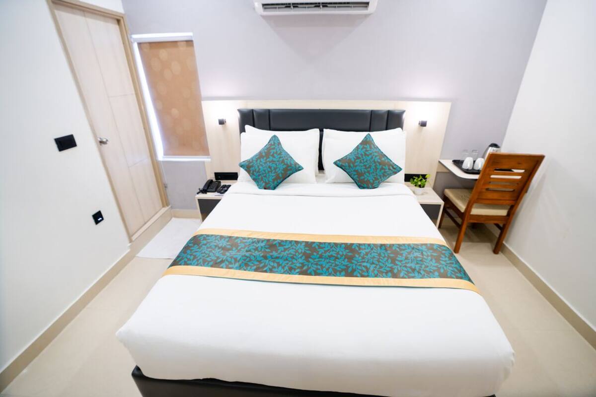Quarto de hotel com cama, mesa de cabeceira, cadeira e escrivaninha.