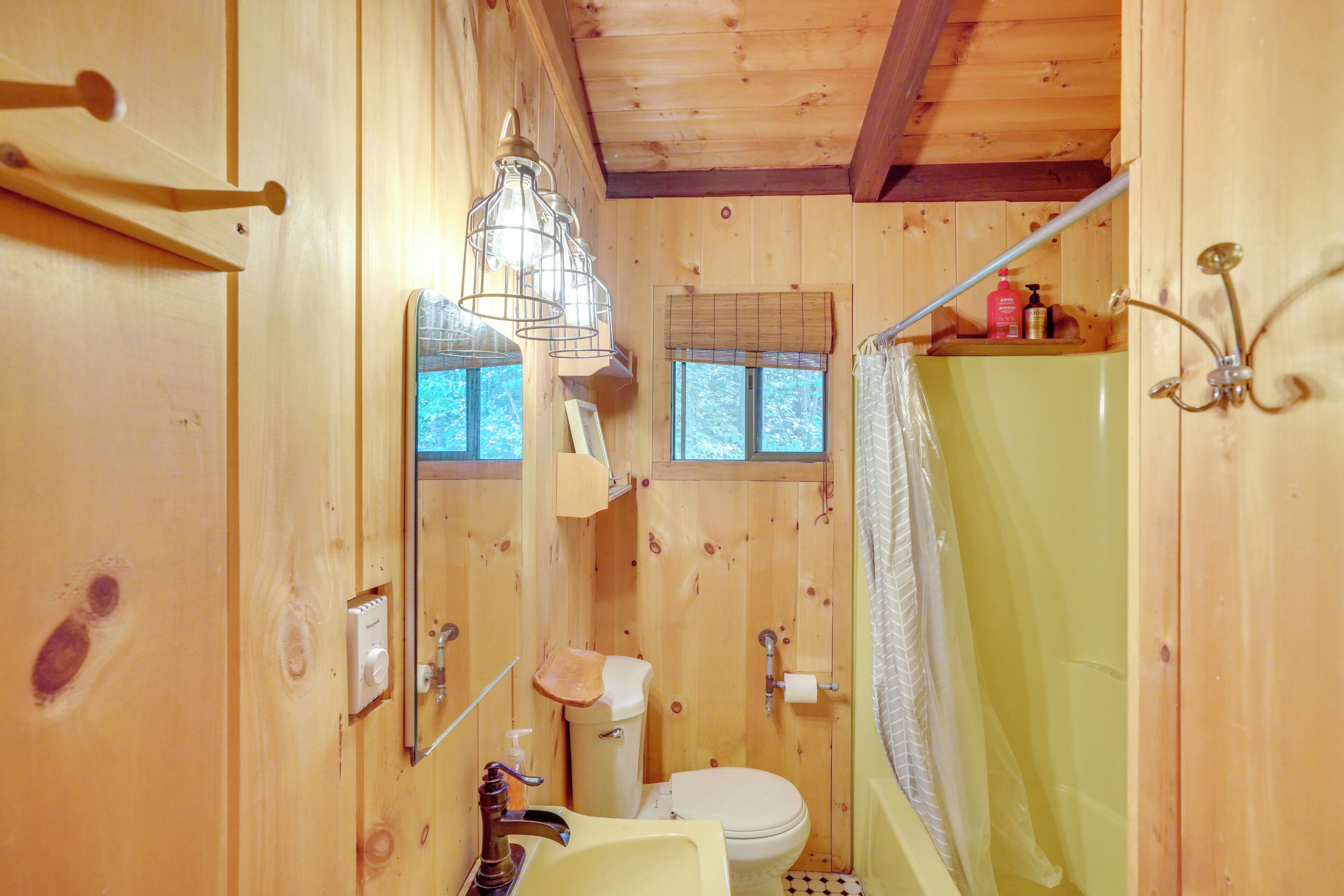 Baño de cabaña de madera con inodoro, lavamanos y cortina de ducha.