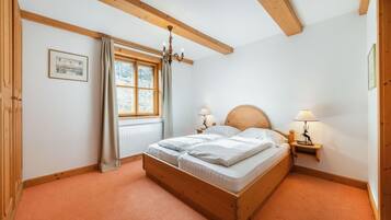 A bedroom with a wooden bed, two bedside tables with lamps, a window with curtains, and a chandelier.