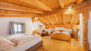 Een ruime kamer met een hoog houten plafond, twee bedden, een bank en een kleine tafel.
