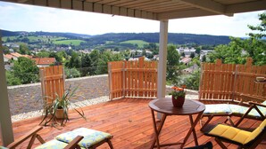 A wooden deck with outdoor furniture, a table, and a view of a town and hills in the background. - Gruppenhaus mit Komfortabler Ausstattung (Regen)