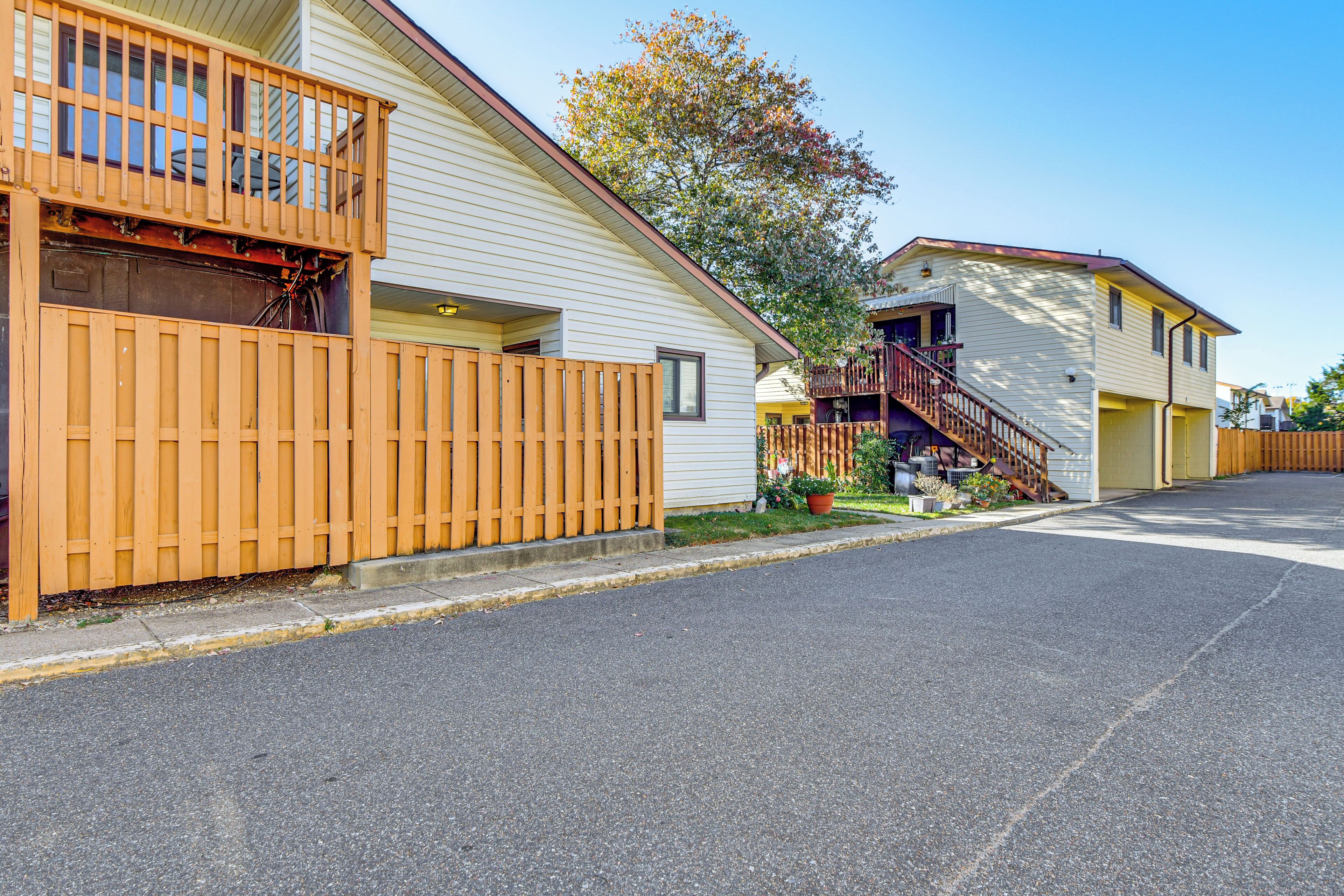 A residential street with two houses, one with a balcony and a wooden fence, and the other with a staircase leading to a porch.