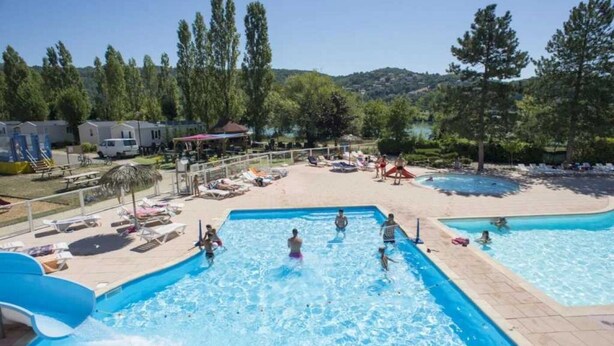 A swimming pool area with multiple pools, lounge chairs, and a water slide.