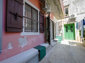 Une ruelle étroite avec un bâtiment rose, une porte verte et un banc blanc.