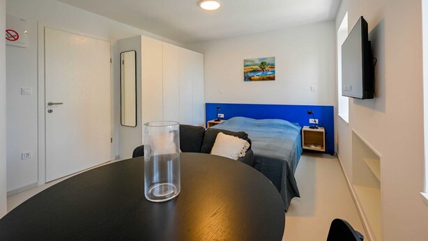 Et hotelværelse med en seng, fjernsyn, et billede, en glassvas og et bord.
