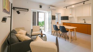 En moderne lejlighed med stue, spiseområde og køkken. Der er en sofa, et spisebord med stole og en køkkenbar.