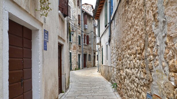 A narrow cobblestone street flanked by stone buildings with wooden shutters and a signboard. - The Quiet Center Apartment in Rovinj (Rovinj)
