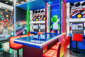 Uma sala de jogos com tema do Mario, com luzes de néon, máquinas de corrida e brinquedos de pelúcia.