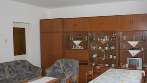 A living room with a sofa, a table with a lace tablecloth, wooden cabinets with glass doors, and a television. - Spacious Crikvenica Apartments With Sea View and Balcony (Crikvenica)