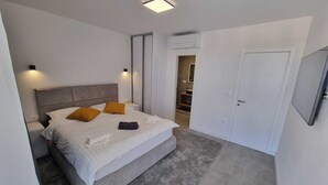 A modern bedroom with a large bed, bedside tables, a wardrobe, and a bathroom visible through an open door. - Sunset Garden Villa in Kanfanar (Kanfanar)