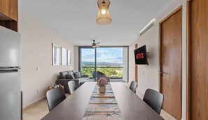 Un espace repas moderne avec une longue table, des chaises, un vase de fleurs, un ventilateur de plafond et un écran de télévision affichant le logo « NETFLIX ».