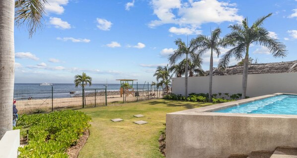 Una piscina, un área verde con palmeras y vista al océano.
