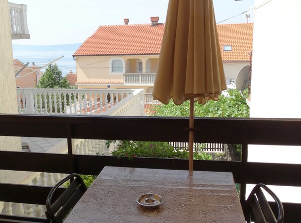 A balcony with a table and chairs, an umbrella, and a view of a building with a red-tiled roof. - Sweet and Simple Sea View Crikvenica Apartments (Crikvenica)