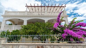 A white building with a covered porch and a stone wall in front. - Modern Villa Near the Sea (Blato)