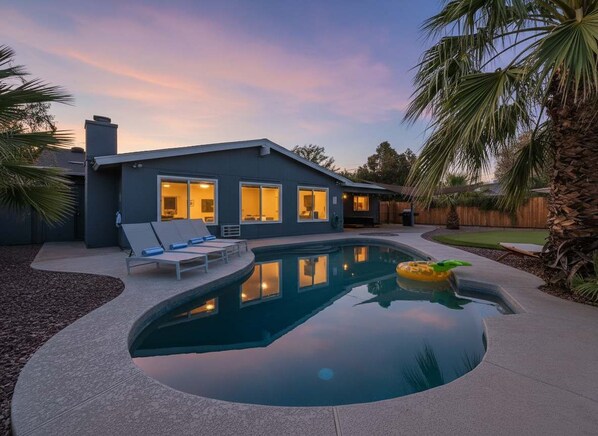A modern house with a swimming pool, a patio with lounge chairs, and a well-maintained lawn.